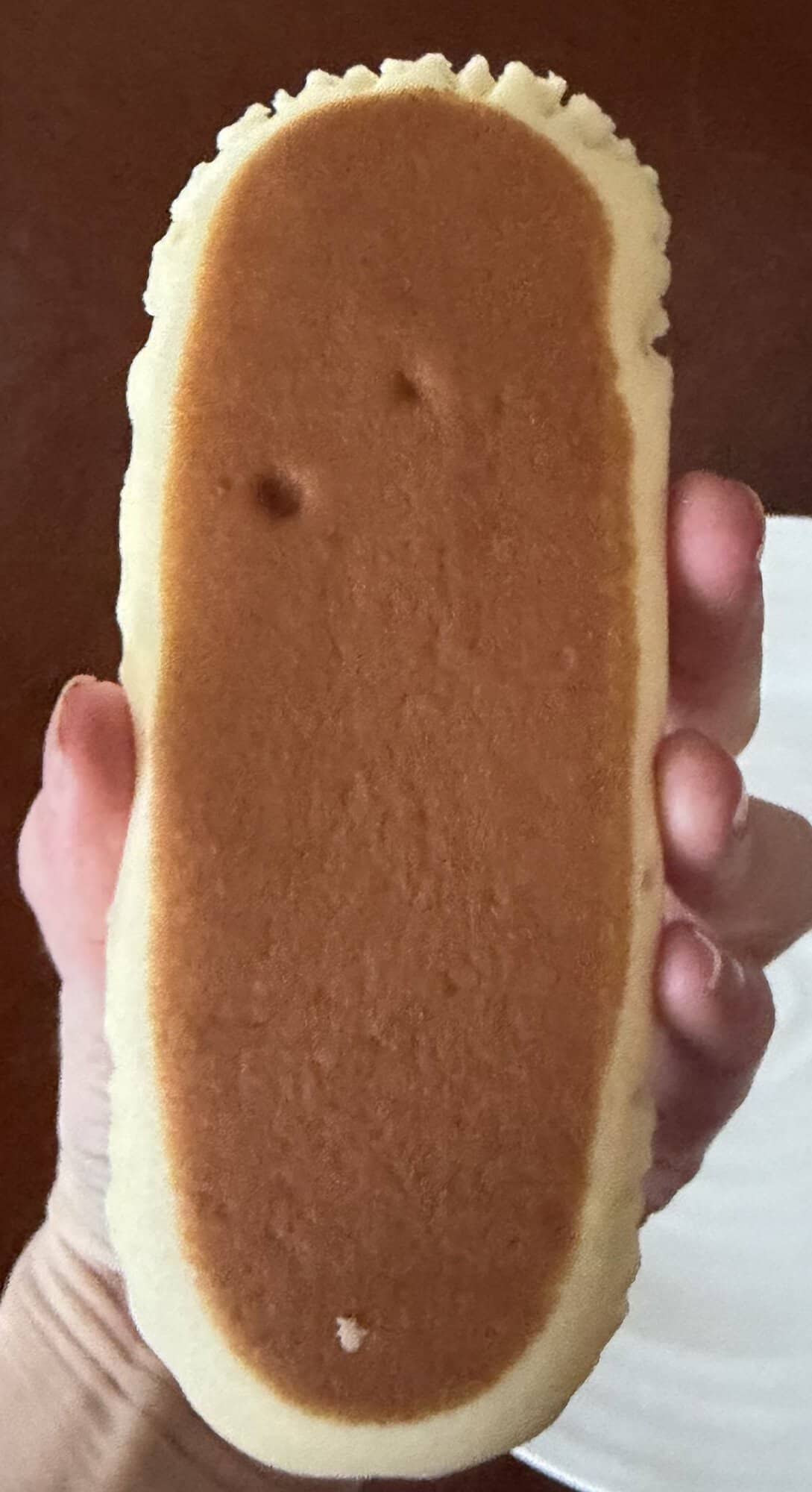 Image of a hand holding a slice of cheesecake close to the camera so you can see the browned top.