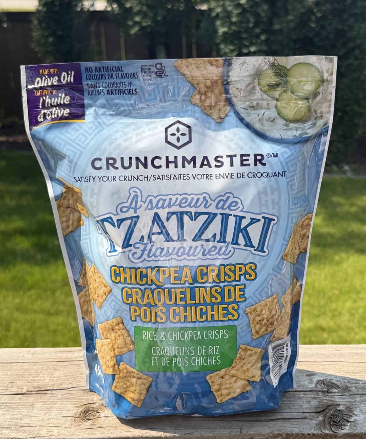 Image of the Costco Crunchmaster Tzatziki Chickpea Crisps bag sitting on a deck outside unopened.