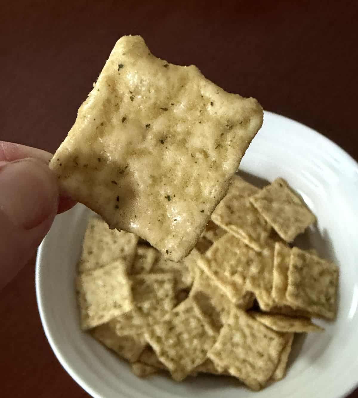 Cloeseup image of a hand holding one tzatziki chickpea crisp close to the camera.