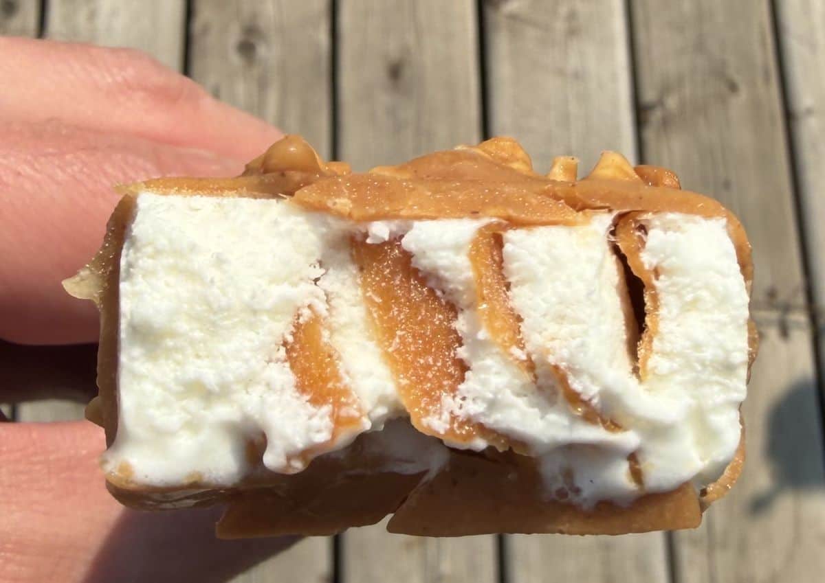 Image of a hand holding one peanut butter ice cream bar with a few bites taken out of it so you can see the center.