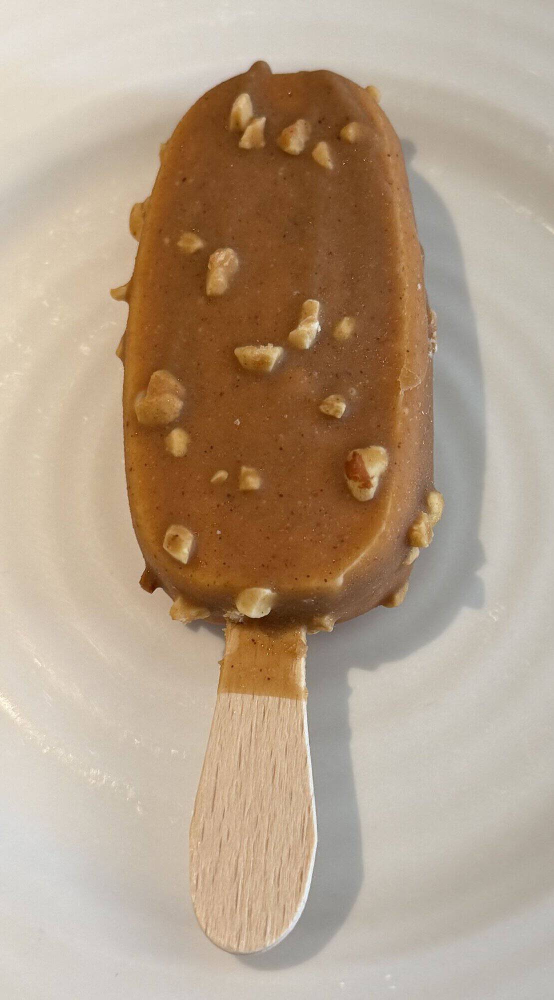 Image of one peanut butter ice cream bar served on a white plate so you can see the crunchy peanut pieces on the coating.