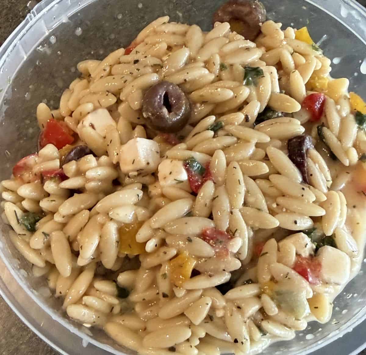 Very close top down image of the orzo salad, there is olives feta and orzo.