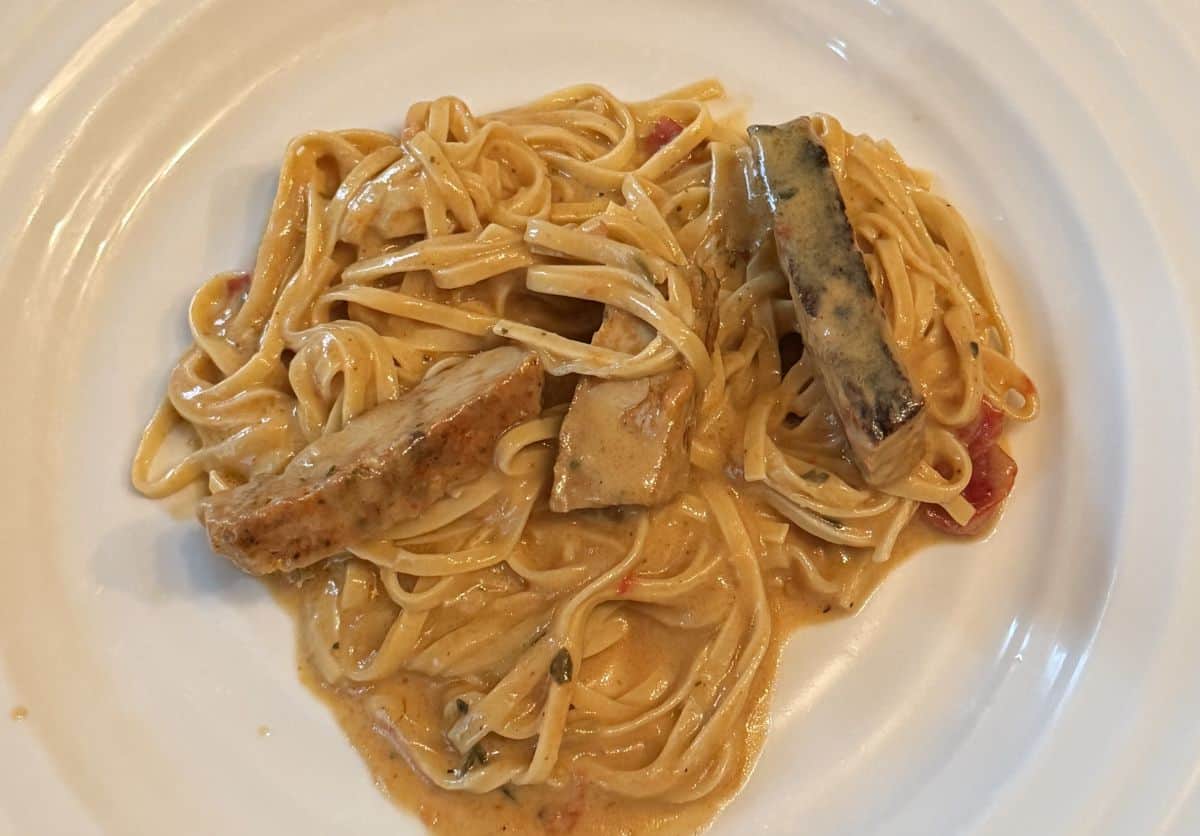 Top down image of the cooked linguine with sauce, sausage and chicken served on a white plate.
