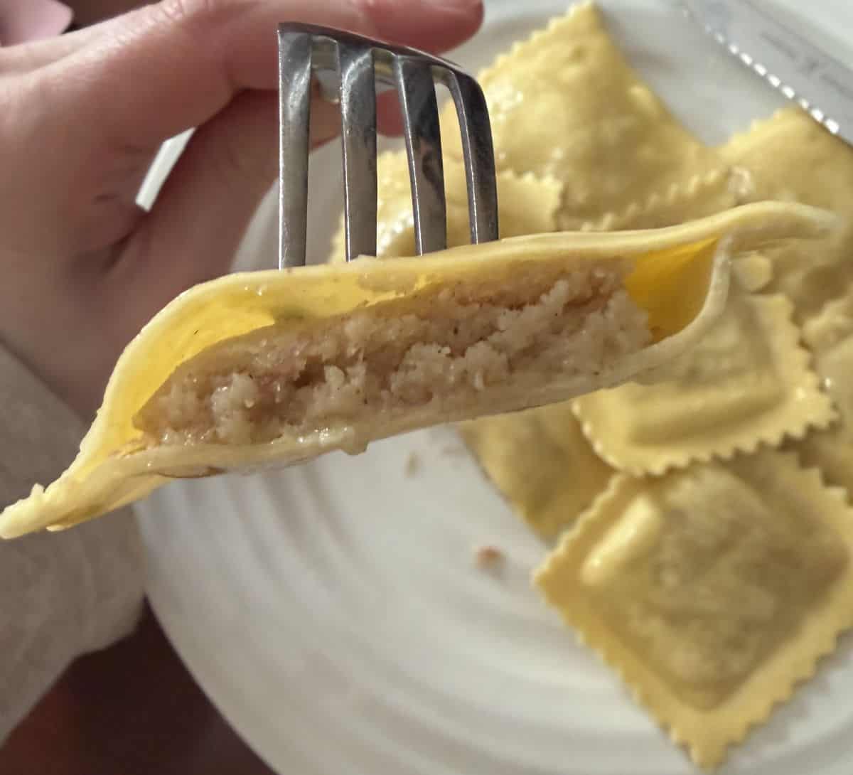 Image of one piece of ravioli being held close to the camera cut in half so you can see the filling inside.