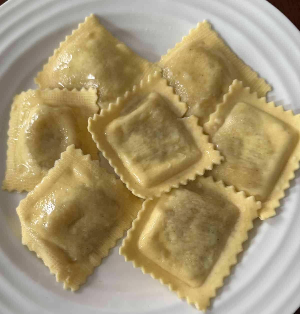 Top down image of a plate of cooked ravioli with butter sauce on it.