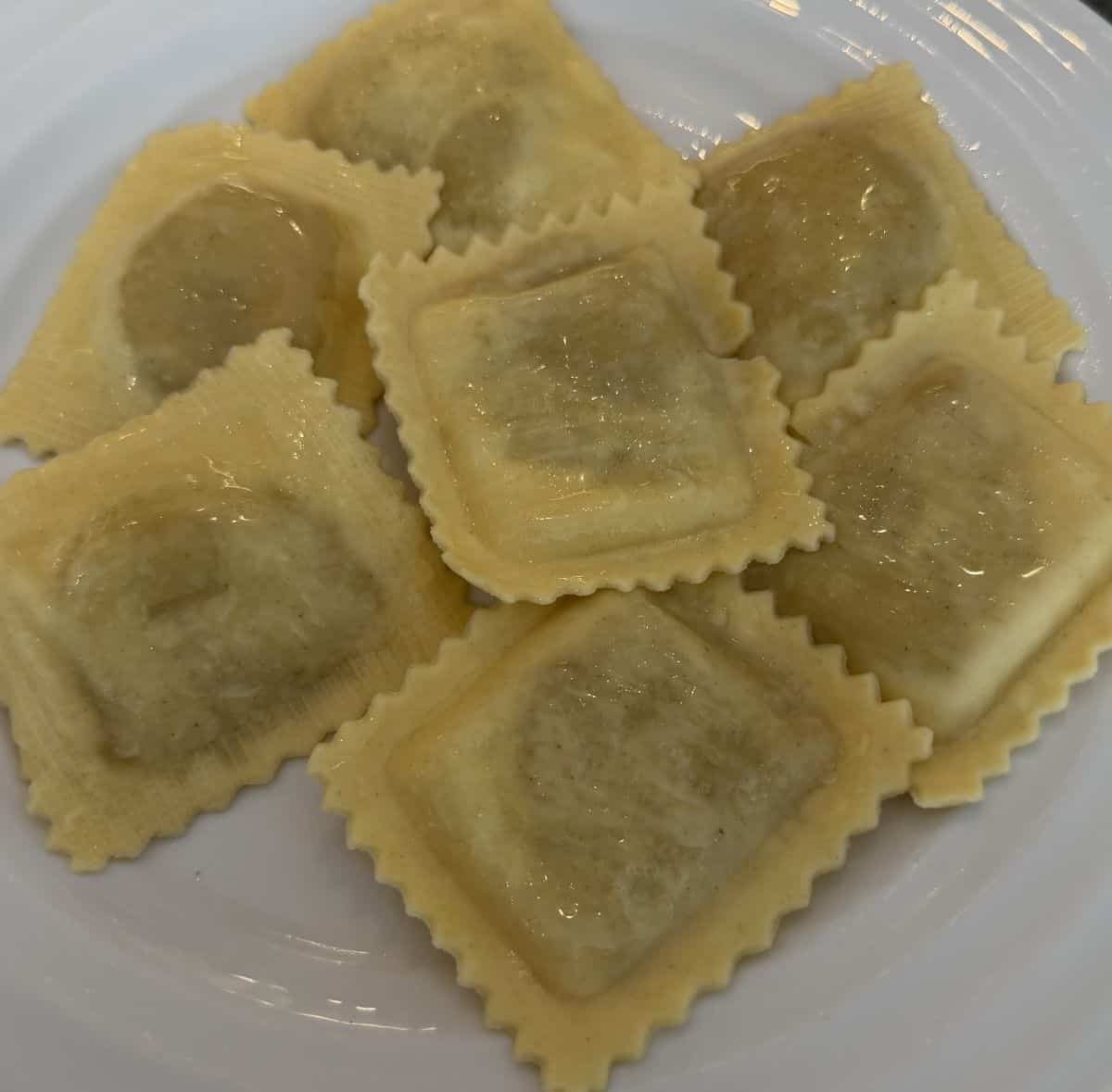 Top down image of the ravioli served on a white plate with olive oil drizzled on top.