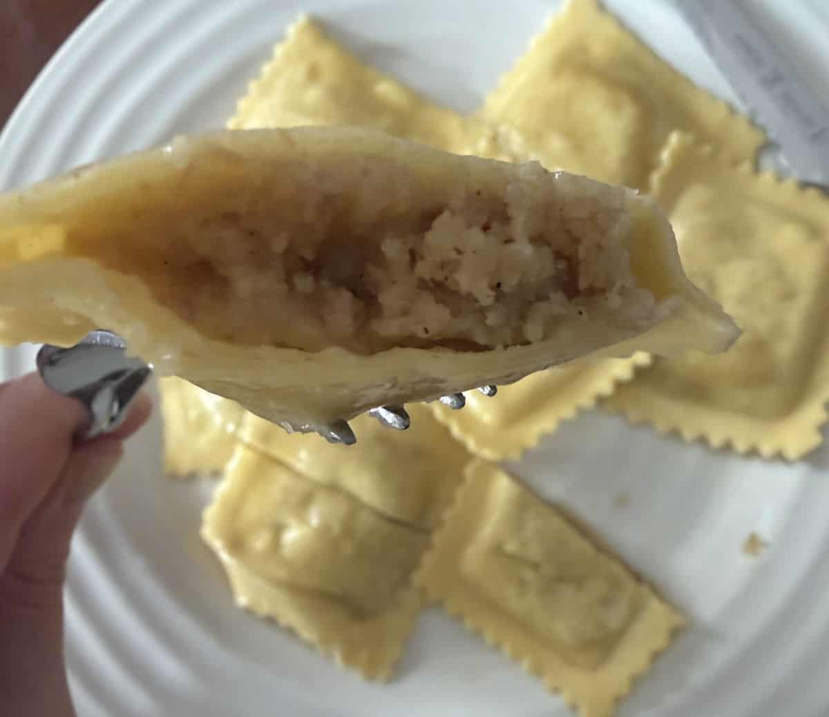 Closeup image of a fork with a piece of ravioli on it cut in half so you can see the filling.