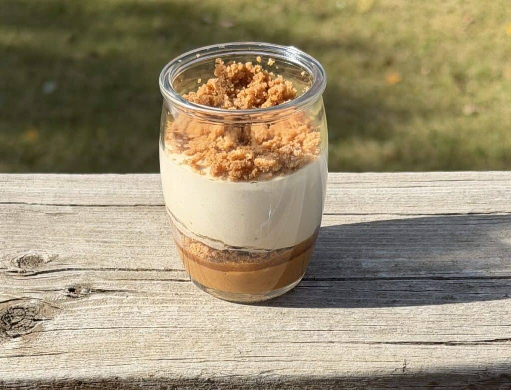 Sideview image of one Delici Cookie Butter Mousse sitting on a deck outside. All the layers in the mousse are visiable.