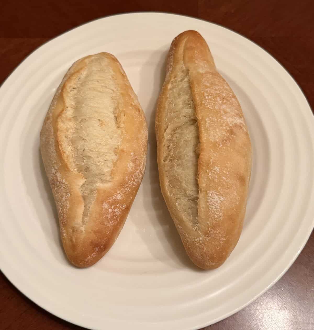 Image of two crusty rolls served on a white plate.