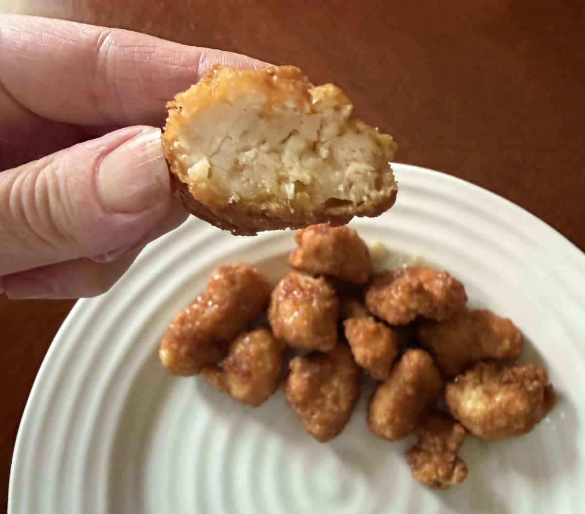 Image of a hand holding one piece of chicken without sauce with a bite taken out so you can see the middle.