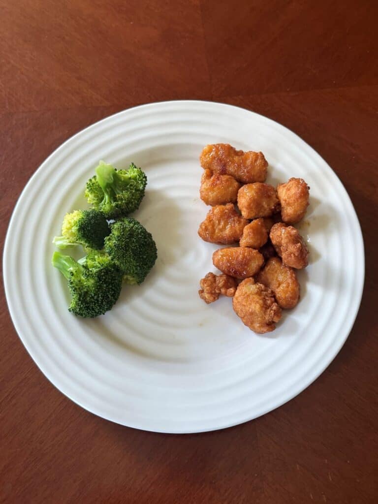 Image of the cooked lemon chicken with sauce served on a white plate beside broccoli.