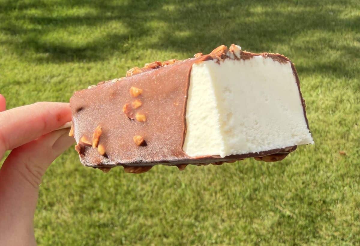Image of a hand holding one vanilla almond ice cream bar with a few bites taken so you can see the center.