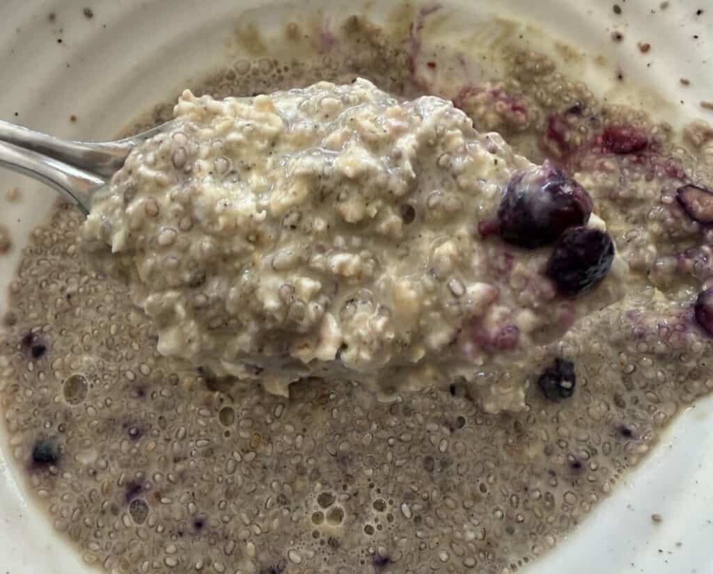 Top down close up image of a spoon hovering over a bowl of overnight oats with oatmeal on it.