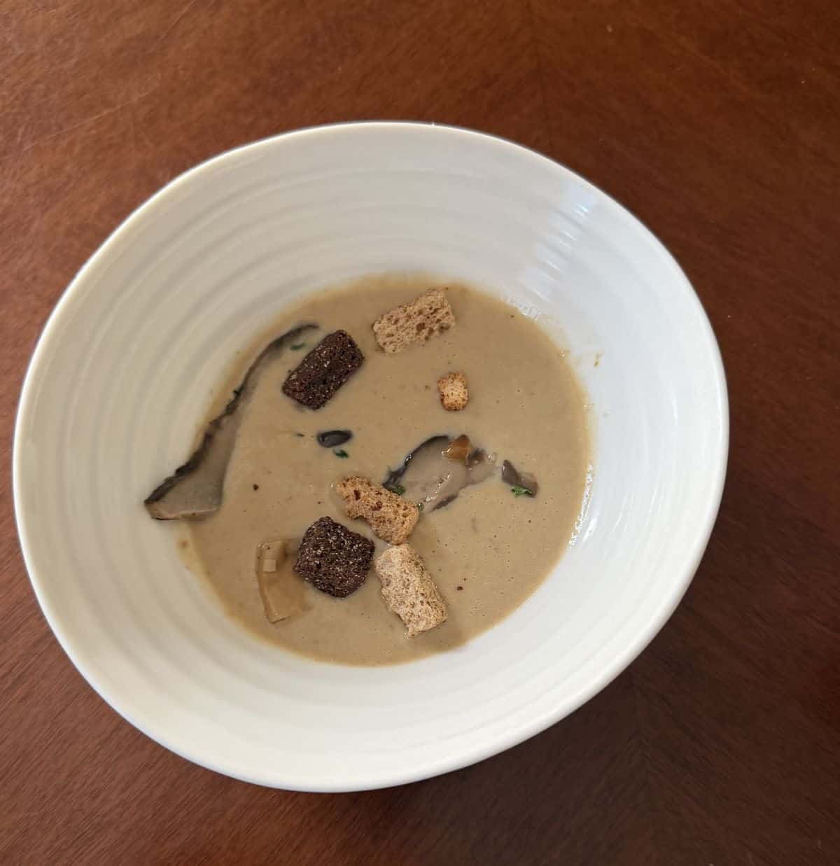 Top down image of the mushroom soup in a bowl with croutons and mushrooms in it.