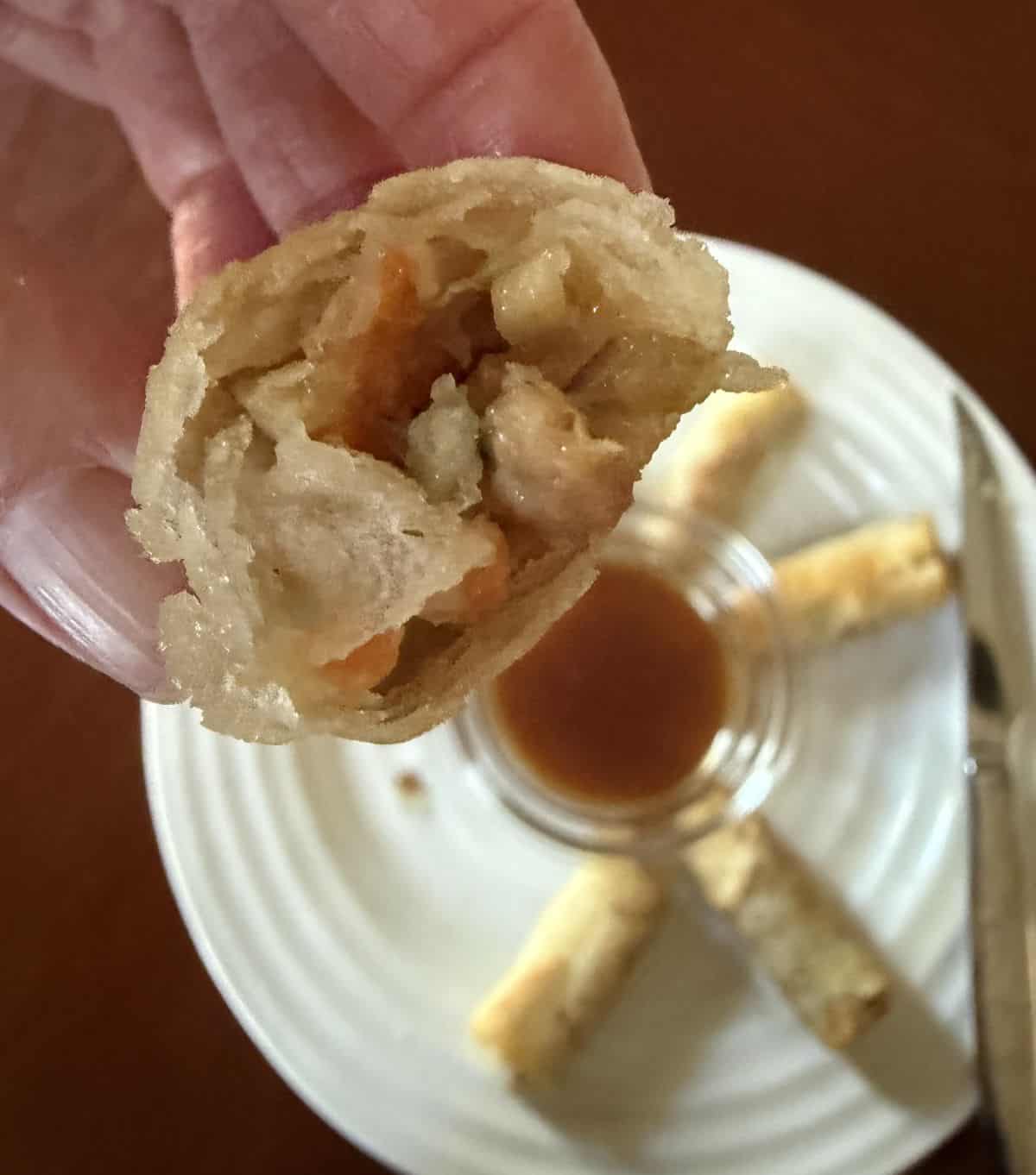 Image of a hand holding one spring roll with a bite taken out of it close to the camera so you can see the filling inside.