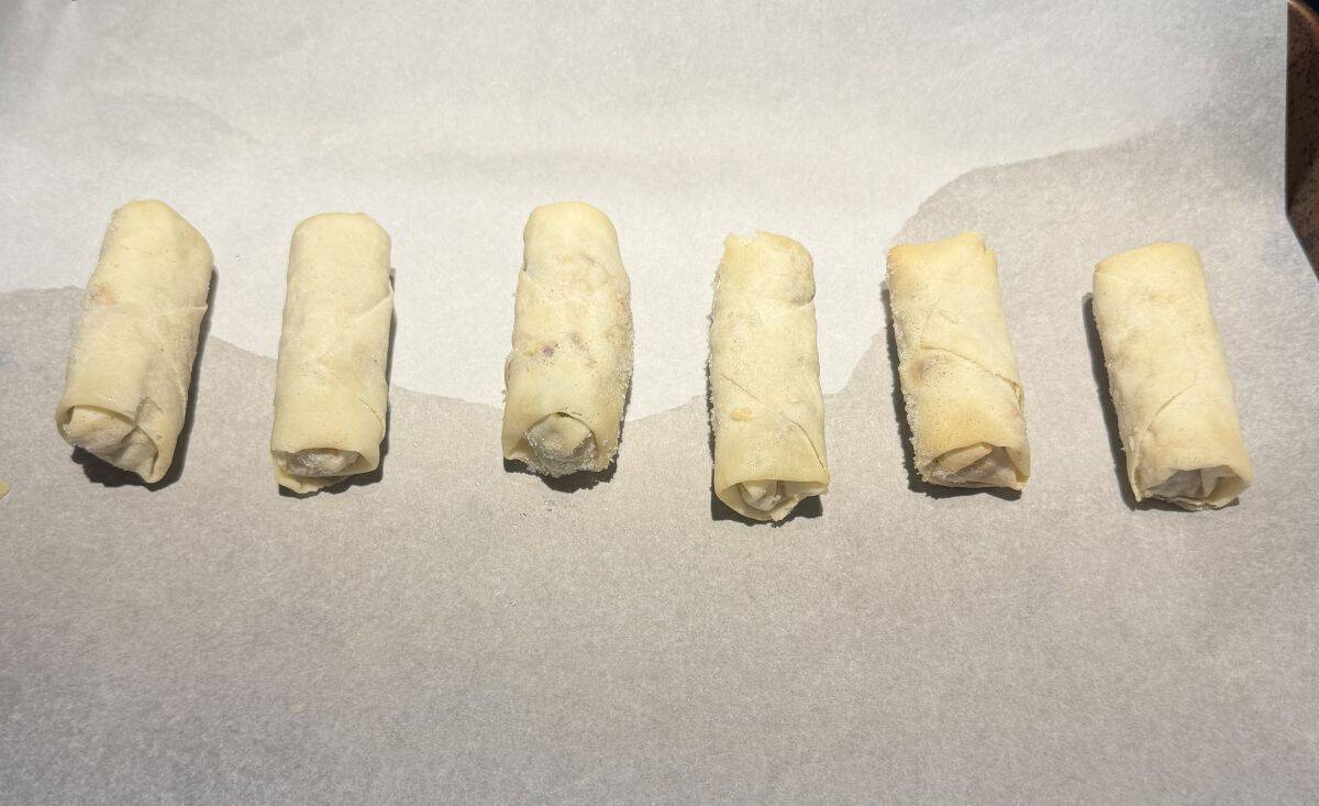 Image of six frozen spring rolls on a baking tray prior to being put in the oven.