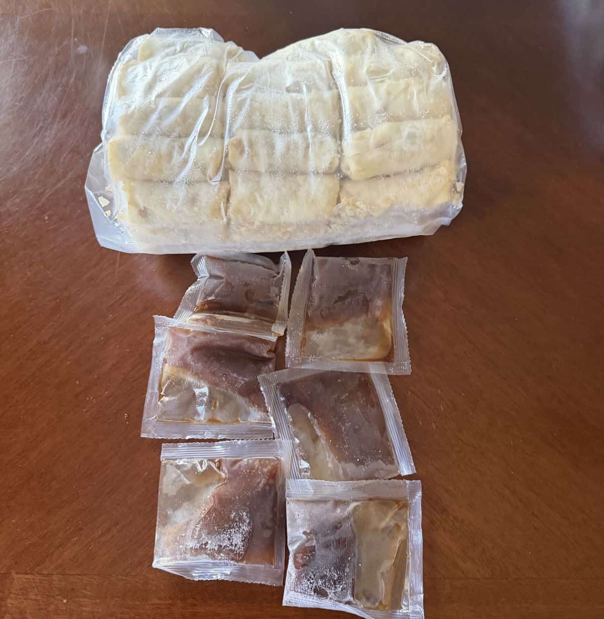Image of a plastic bag of frozen spring rolls with six packets of sauce beside it. all unopened.