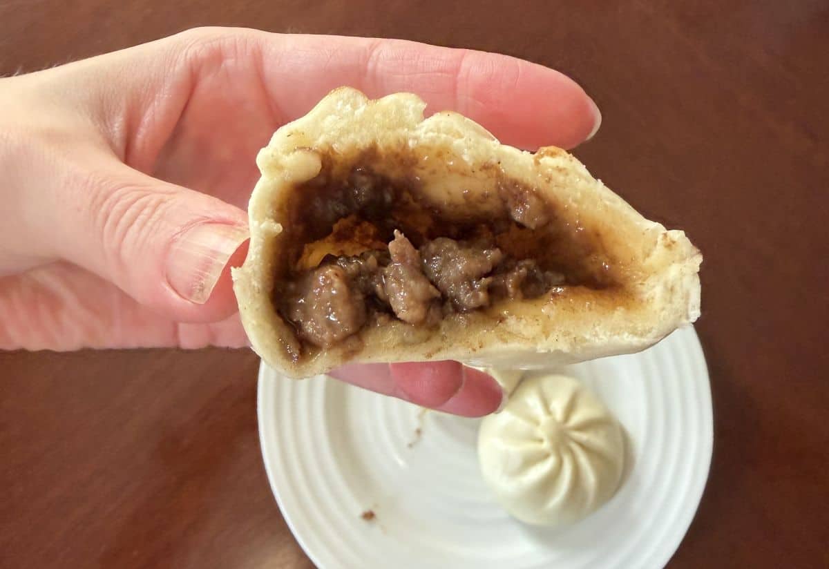 Image of a hand holding one pork bao bun with a few bites taken out so you can see the filling.