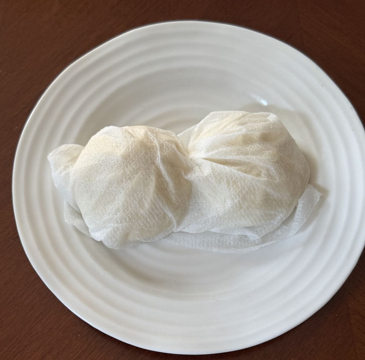 Two pork bao buns wrapped in damp paper towel before heating them in the microwave.