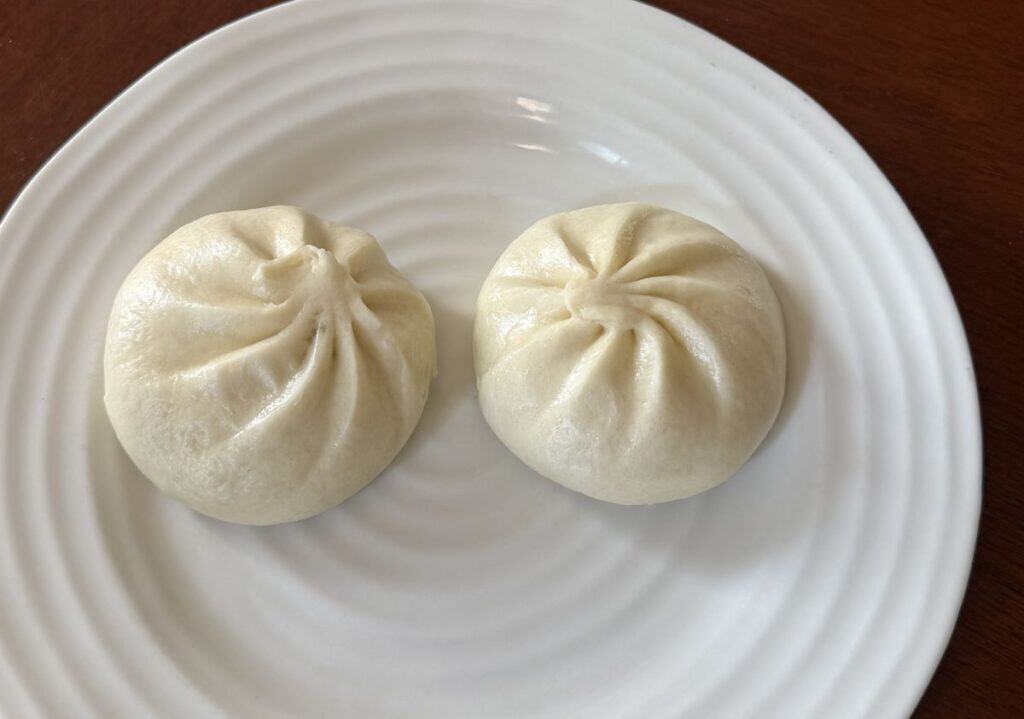 Image of two cooked pork bao buns served on a white plate.