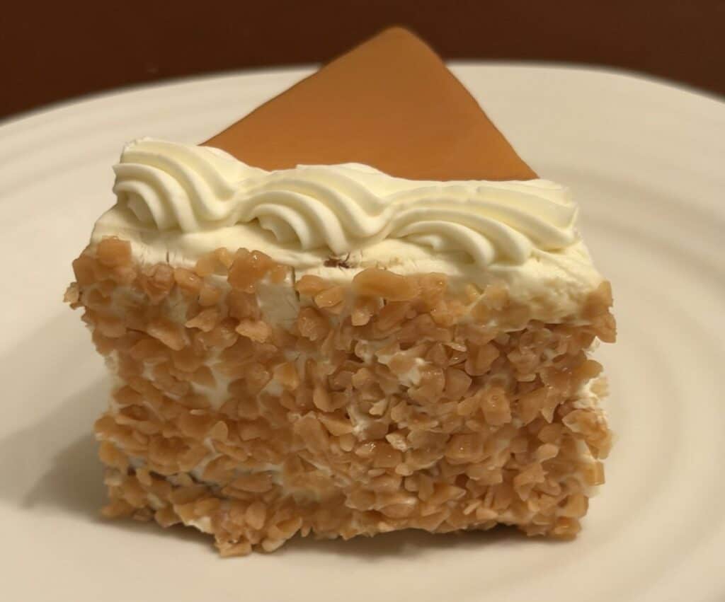 Side view image of the outside of one slice of cake showing whipped cream and toffee crumble.