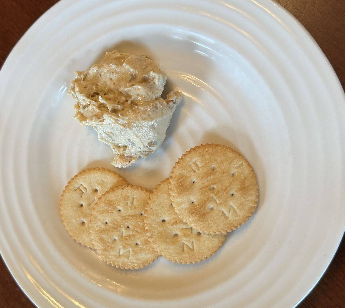 Closeup top-down image of a serving of dip beside four crackers served on a white plate.