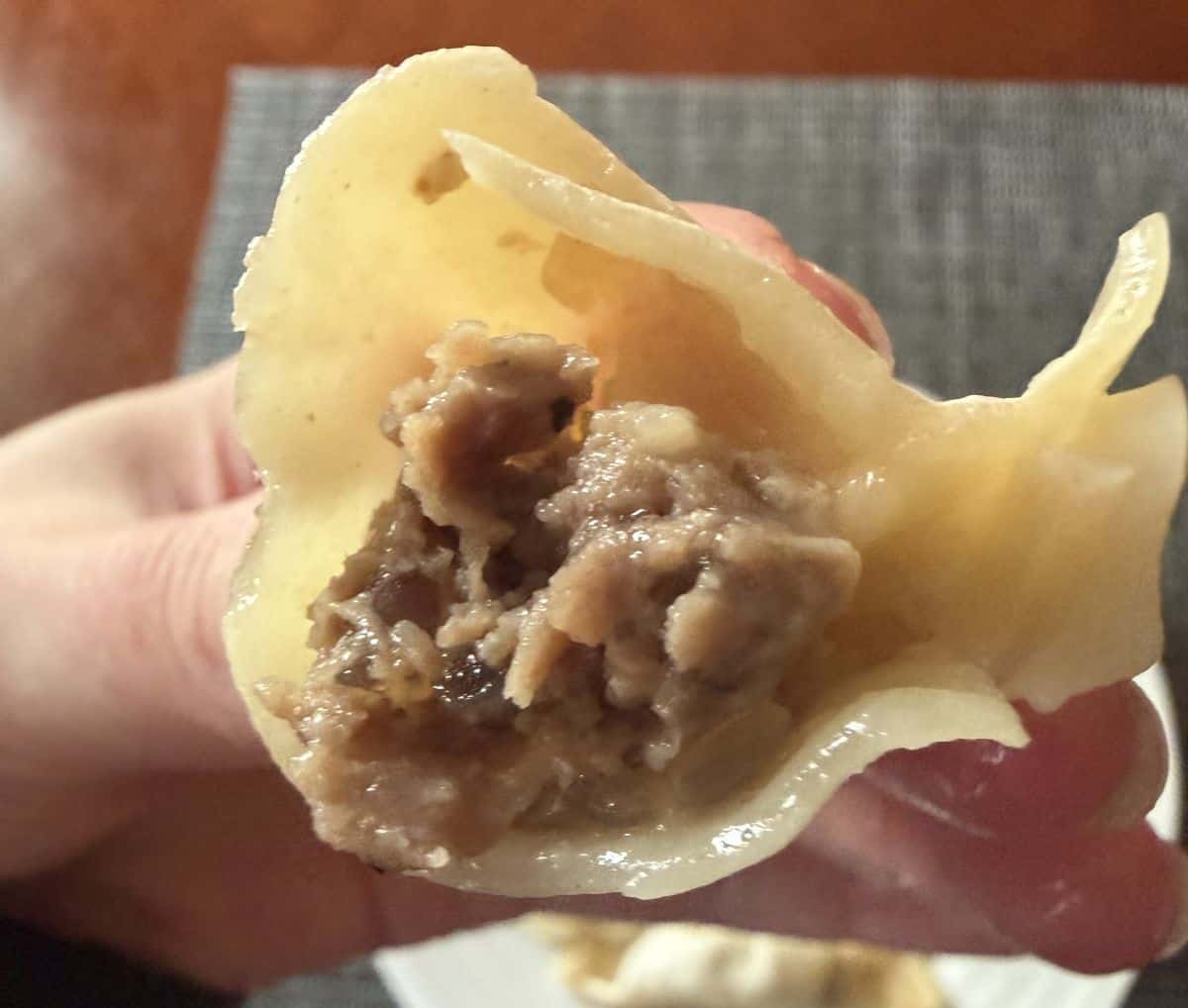 Image of a hand holding one gyoza close to the camera with a bite taken out so you can see the filling inside.