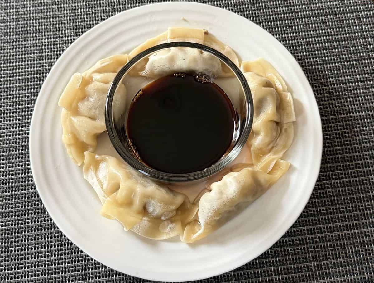 Image of cooked gyoza served on a white plate with soy sauce in a bowl in the middle.