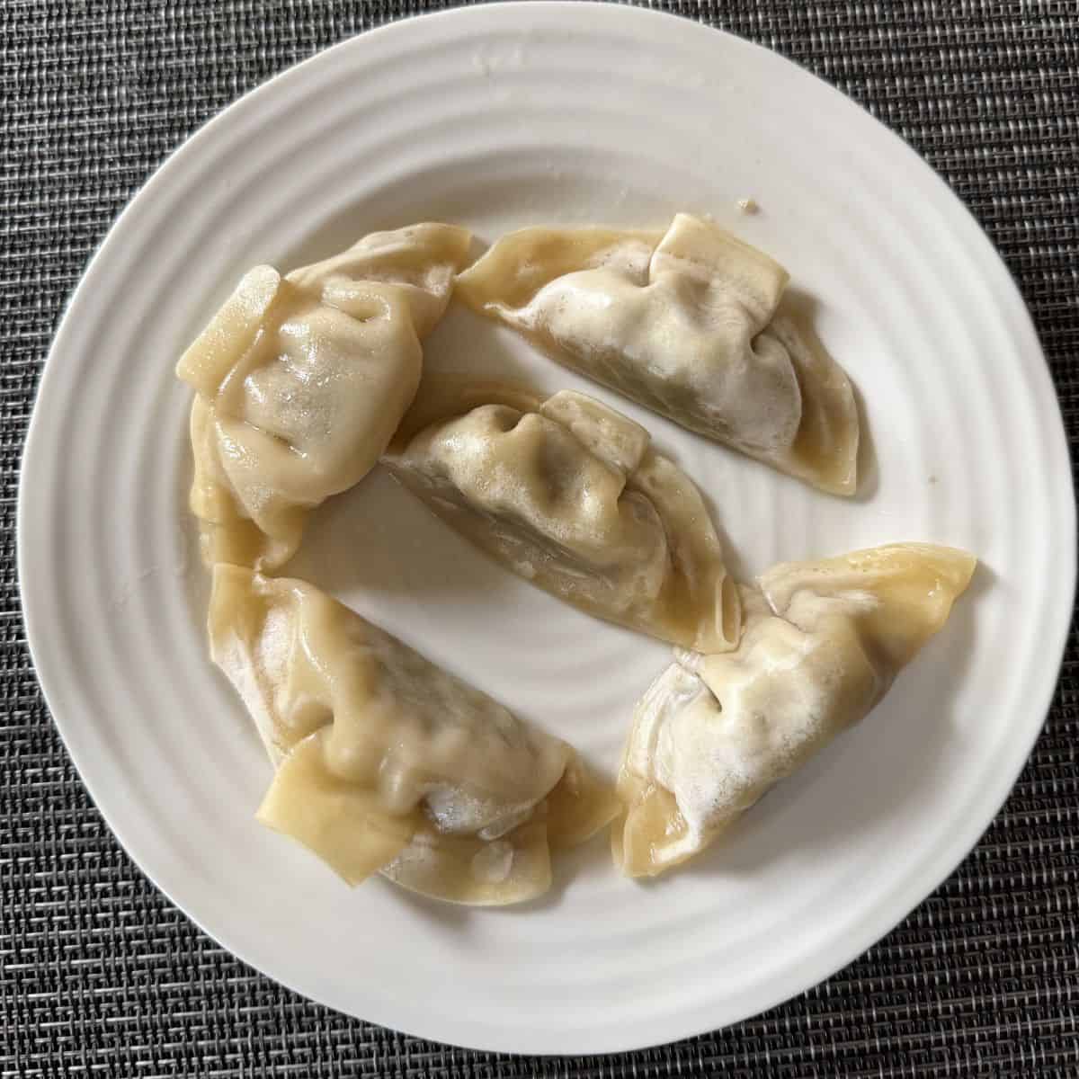 Image of five cooking gyoza served on a white plate.