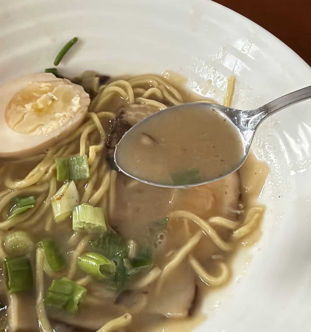 Closeup image of a bowl of the ramen with a spoon hovering over the bowl with broth on it.