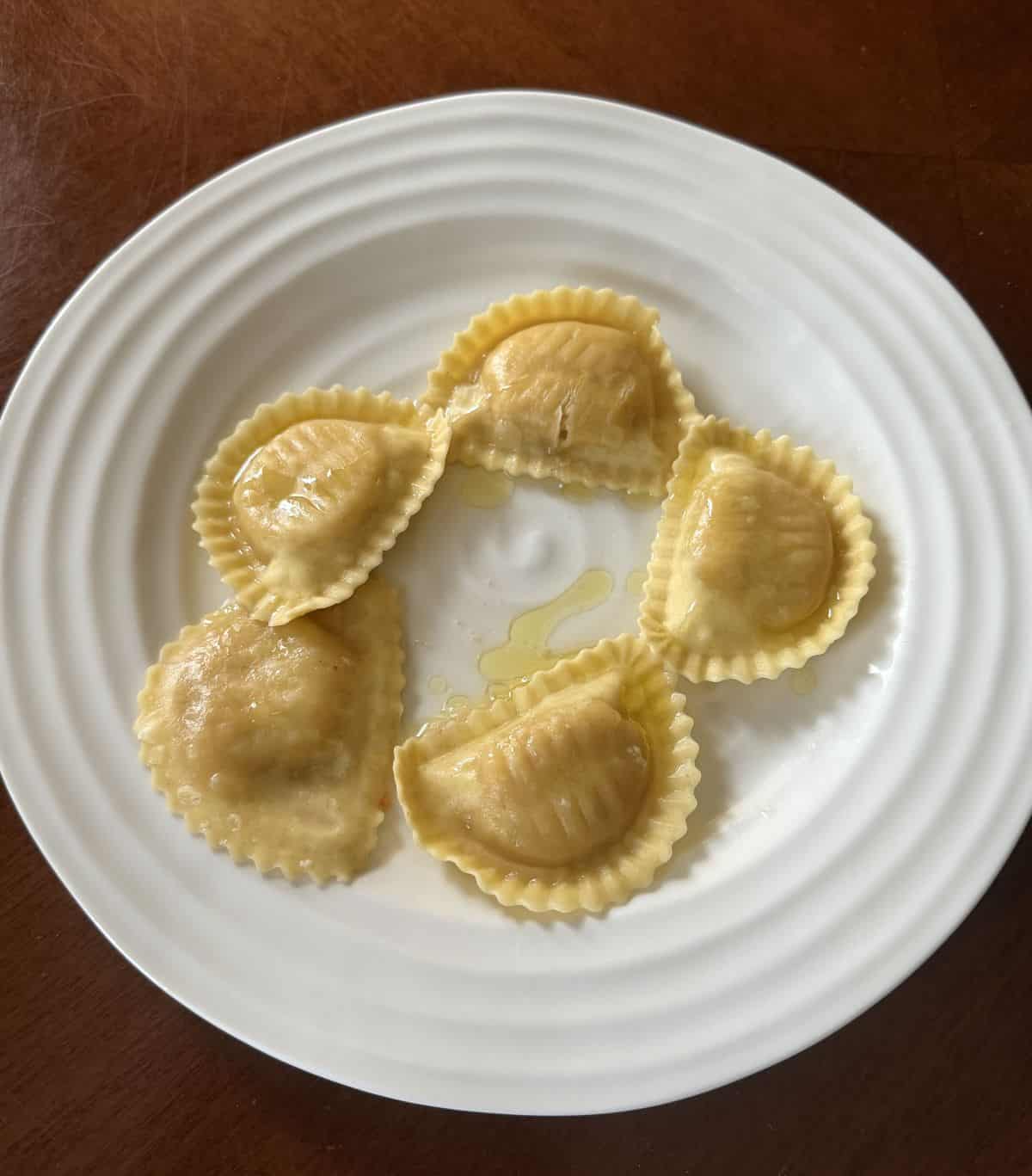 Top down image of the ravioli cooked and served on a white plate with olive oil on it.