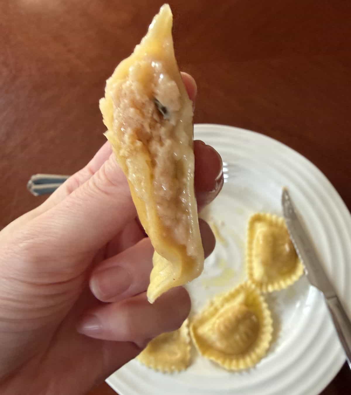 Image of a hand holding one piece of ravioli that's been cut in half so you can see the filling inside.